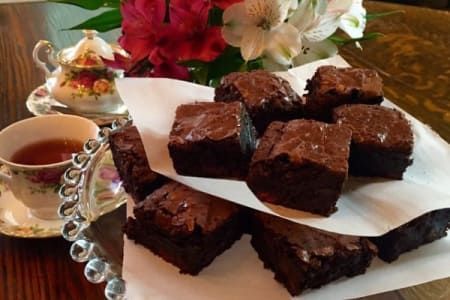 Brownies on parchment, tea in floral cup, flowers and teapot in background.