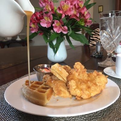 Chicken and waffles with syrup being poured, flowers in background.