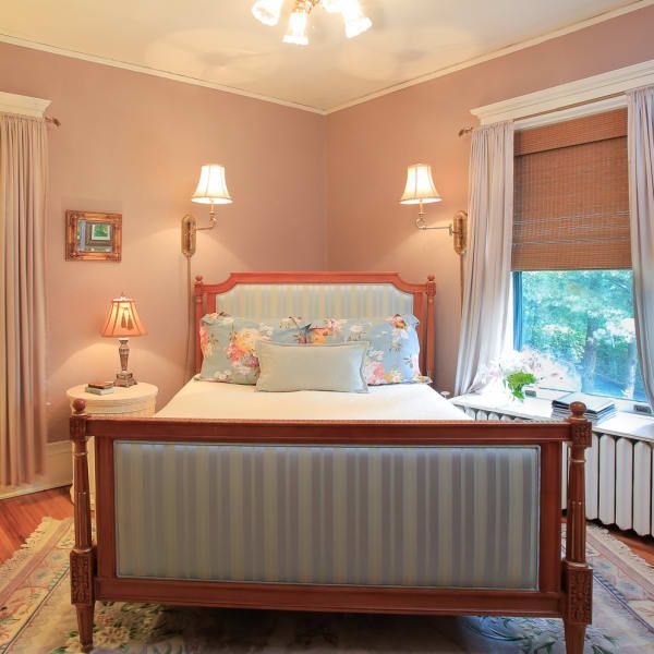 Bedroom with pink walls, wooden bed, striped headboard, and window with curtains.