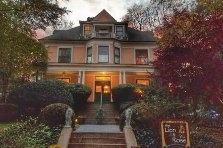 Victorian house with stairs, porch, and sign that reads “Lion & the Rose”.
