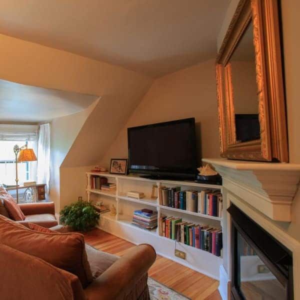 Living room with TV, built-in bookshelves, fireplace, and mirror. Orange sofa, wooden floor, cream walls.