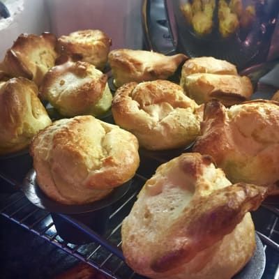 Golden-brown Yorkshire puddings baking on a rack in an oven, slightly overlapping.