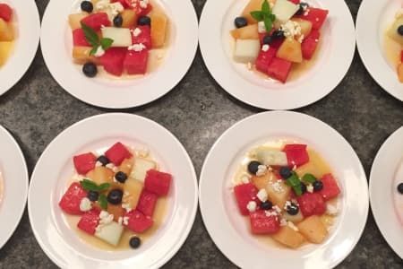 Plates of fruit salad with watermelon, cantaloupe, blueberries, and cheese, garnished with mint.