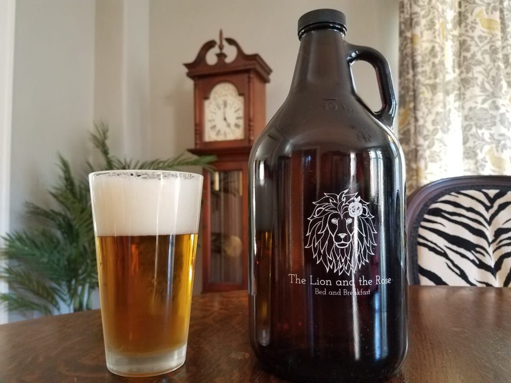 Glass of beer and a brown growler on a table, with a clock and a window in the background.