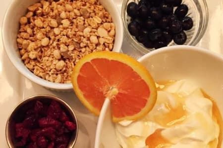 Granola, blueberries, orange slice, cranberries, and yogurt with honey in bowls.