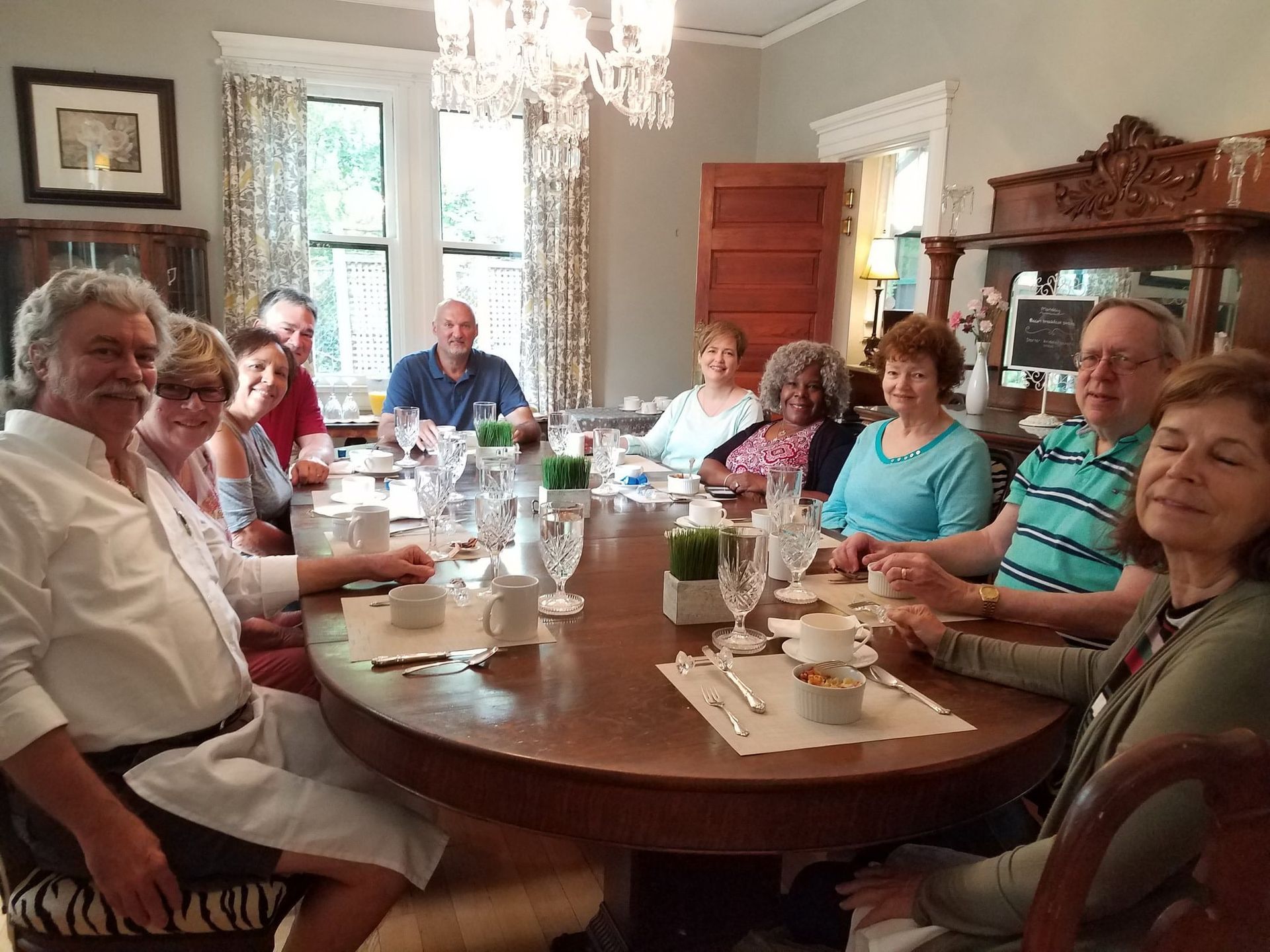 People seated around a large table, presumably dining. Room with chandelier and ornate furniture.