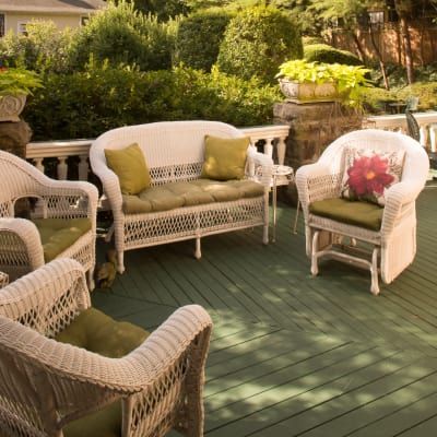Wicker patio furniture with green cushions on a green wooden deck, surrounded by greenery.