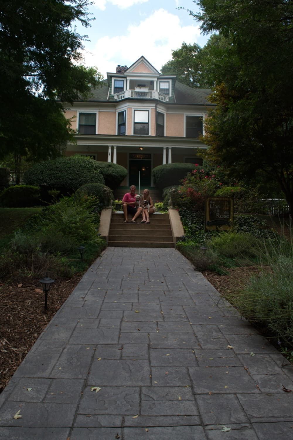 People on steps of a large pink house with a garden path leading toward it.