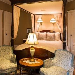 Bedroom with canopy bed, two patterned armchairs, and a lamp on a side table.