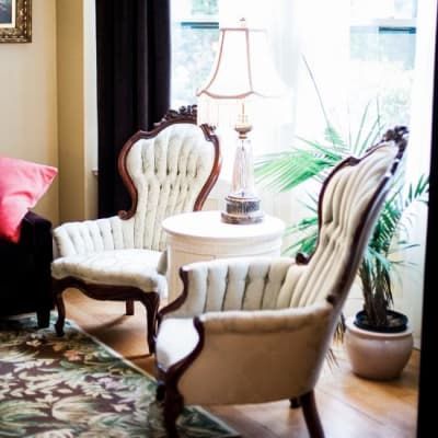 Two ornate armchairs near a small table with a lamp, a houseplant, and a window.