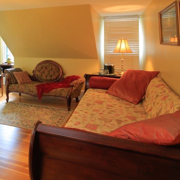 Cozy bedroom with two antique chaise lounges, warm colors, natural light, and a patterned rug.