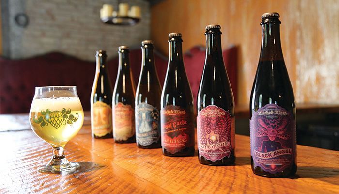A glass of beer and six labeled beer bottles on a wooden table.