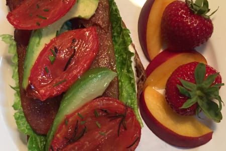 Open-faced sandwich with tomatoes, avocado, and side of peaches and strawberries on a white plate.