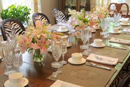 Formal dining table set for a meal. Zebra-print chairs surround a wood table with floral centerpieces and crystal glassware.