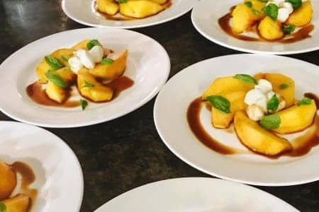 Plates of peach slices with mozzarella, basil, and balsamic glaze on a dark surface.