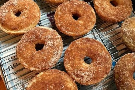 Close-up of cinnamon sugar donuts cooling on a wire rack over a newspaper.