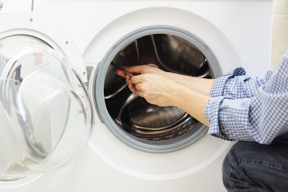 A person is fixing a washing machine with a wrench.