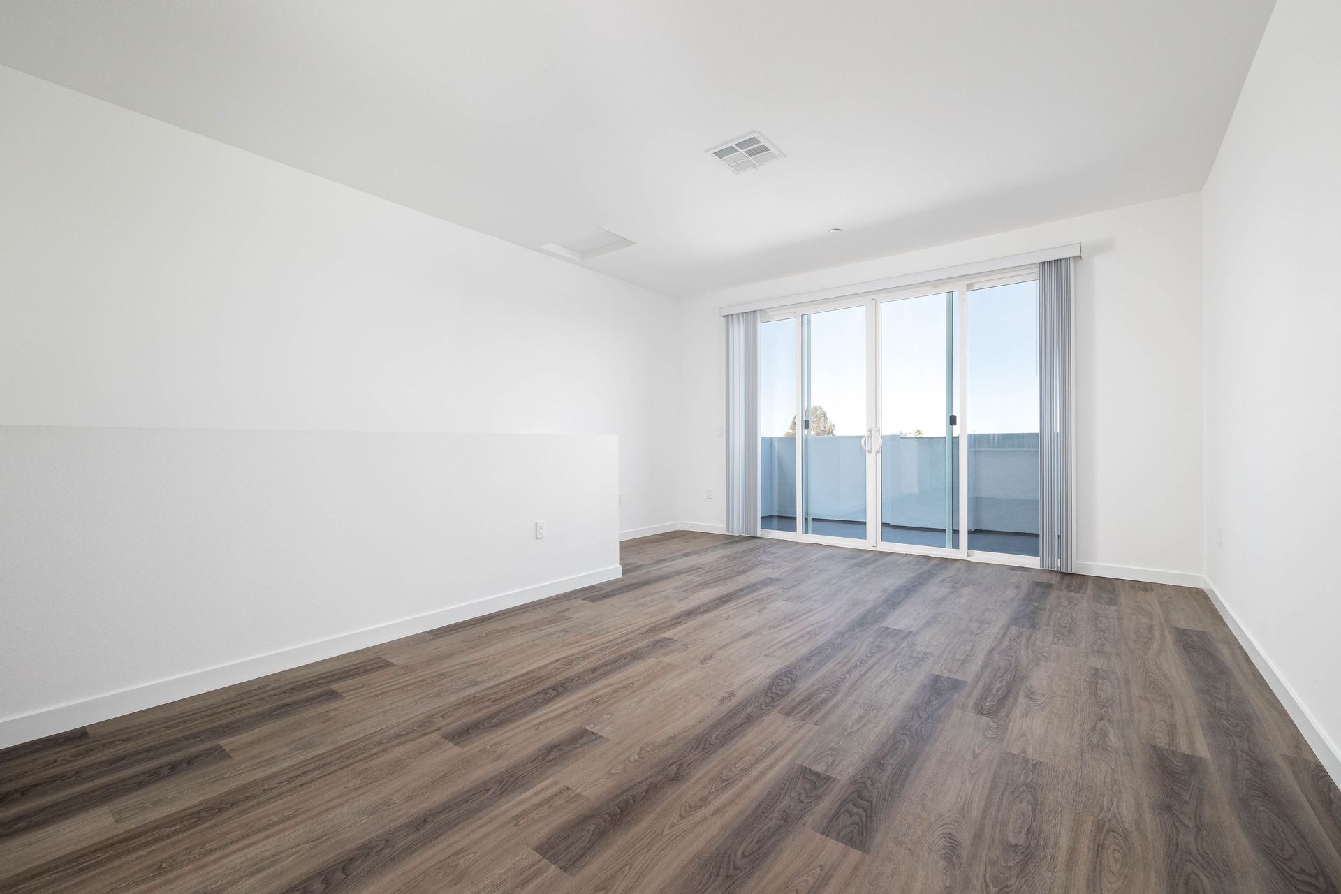 an empty living room with hardwood floors and sliding glass doors leading to a balcony .