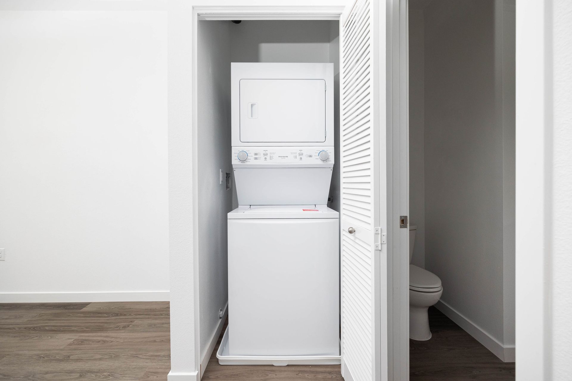 a washer and dryer are stacked in a closet next to a toilet .