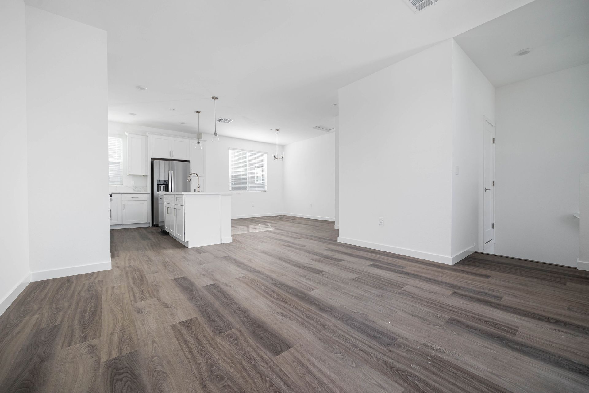an empty living room with hardwood floors and a kitchen in the background .