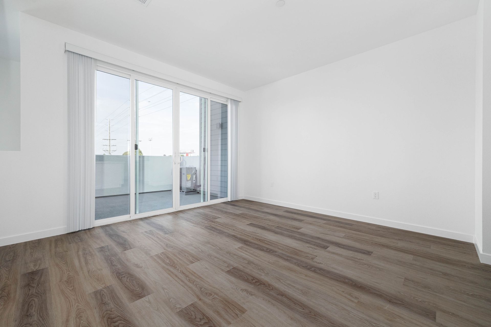 an empty living room with hardwood floors and sliding glass doors leading to a balcony .