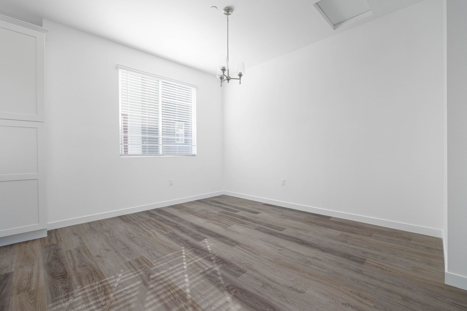 an empty room with hardwood floors , white walls and a window .