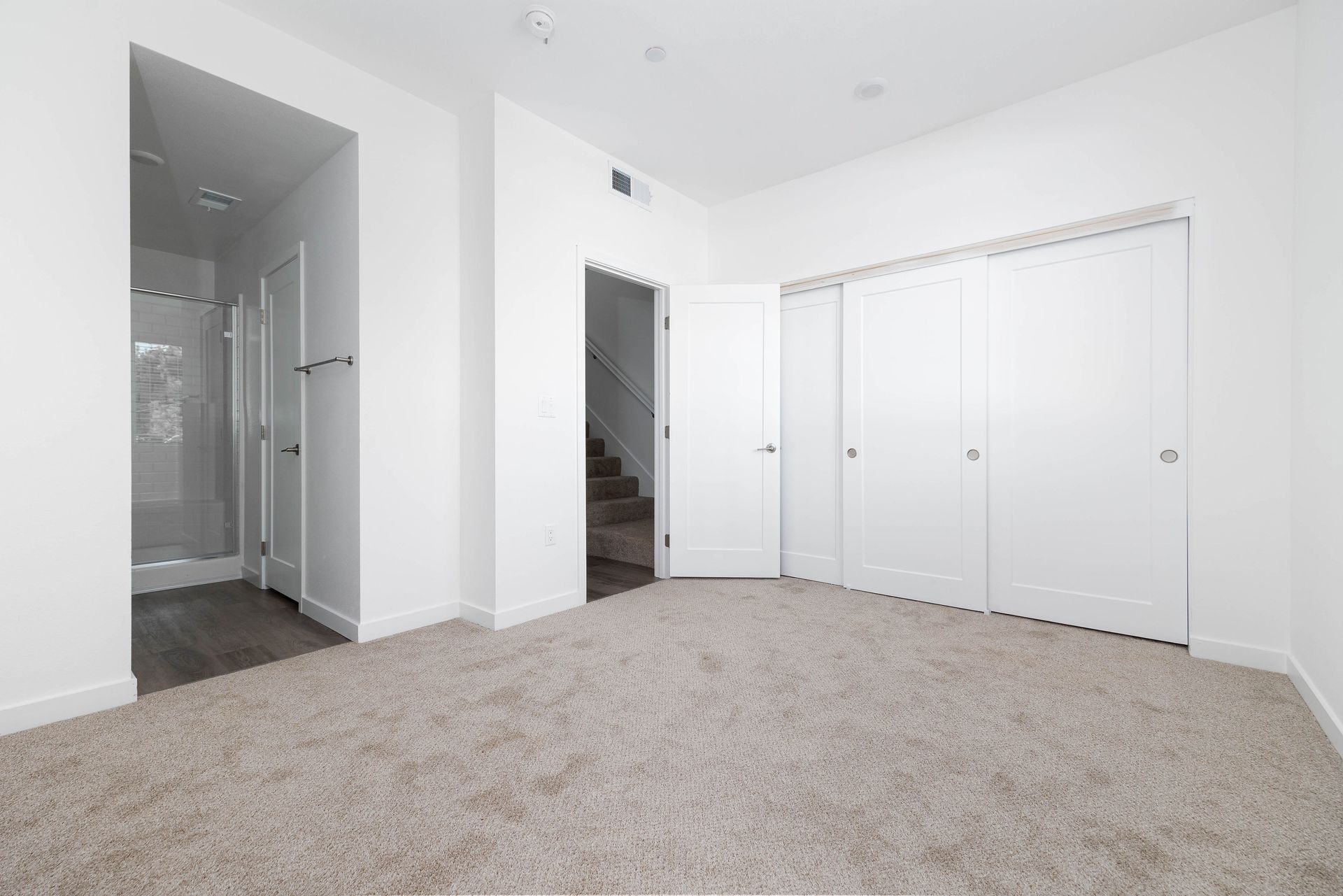 an empty bedroom with a carpeted floor , white walls and closets .