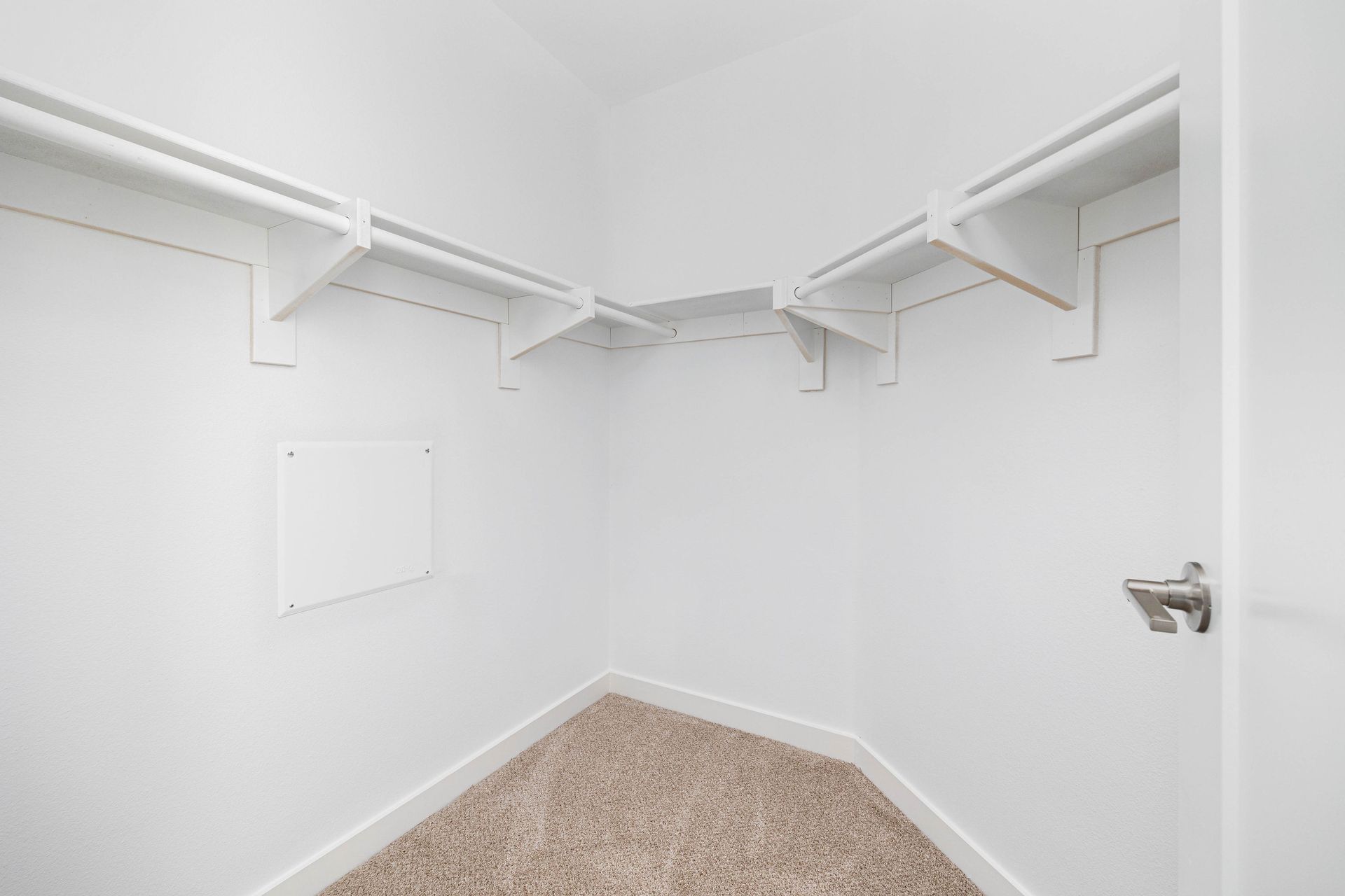 an empty walk in closet with white shelves and a door .