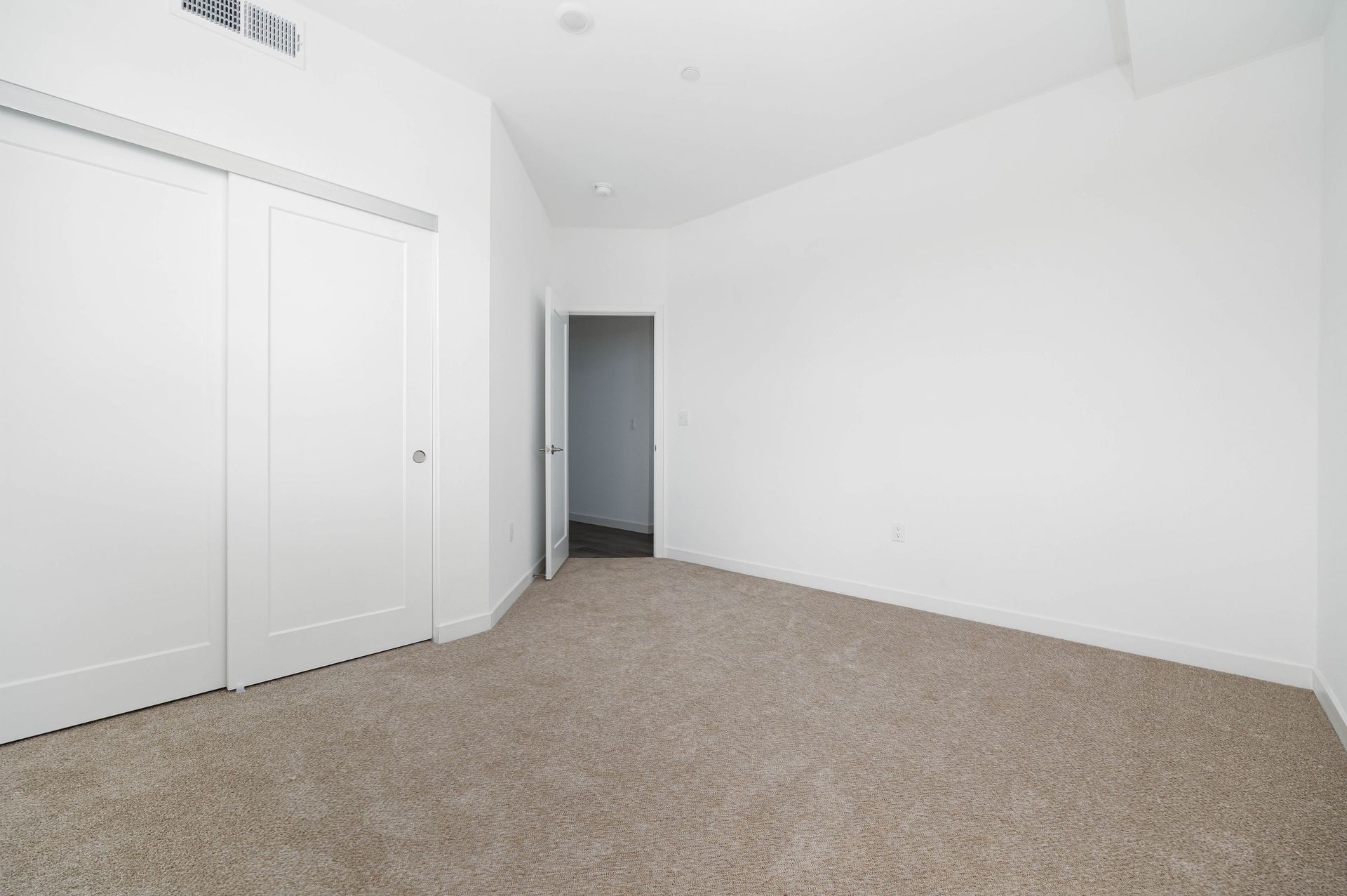 an empty bedroom with a carpeted floor and white walls .