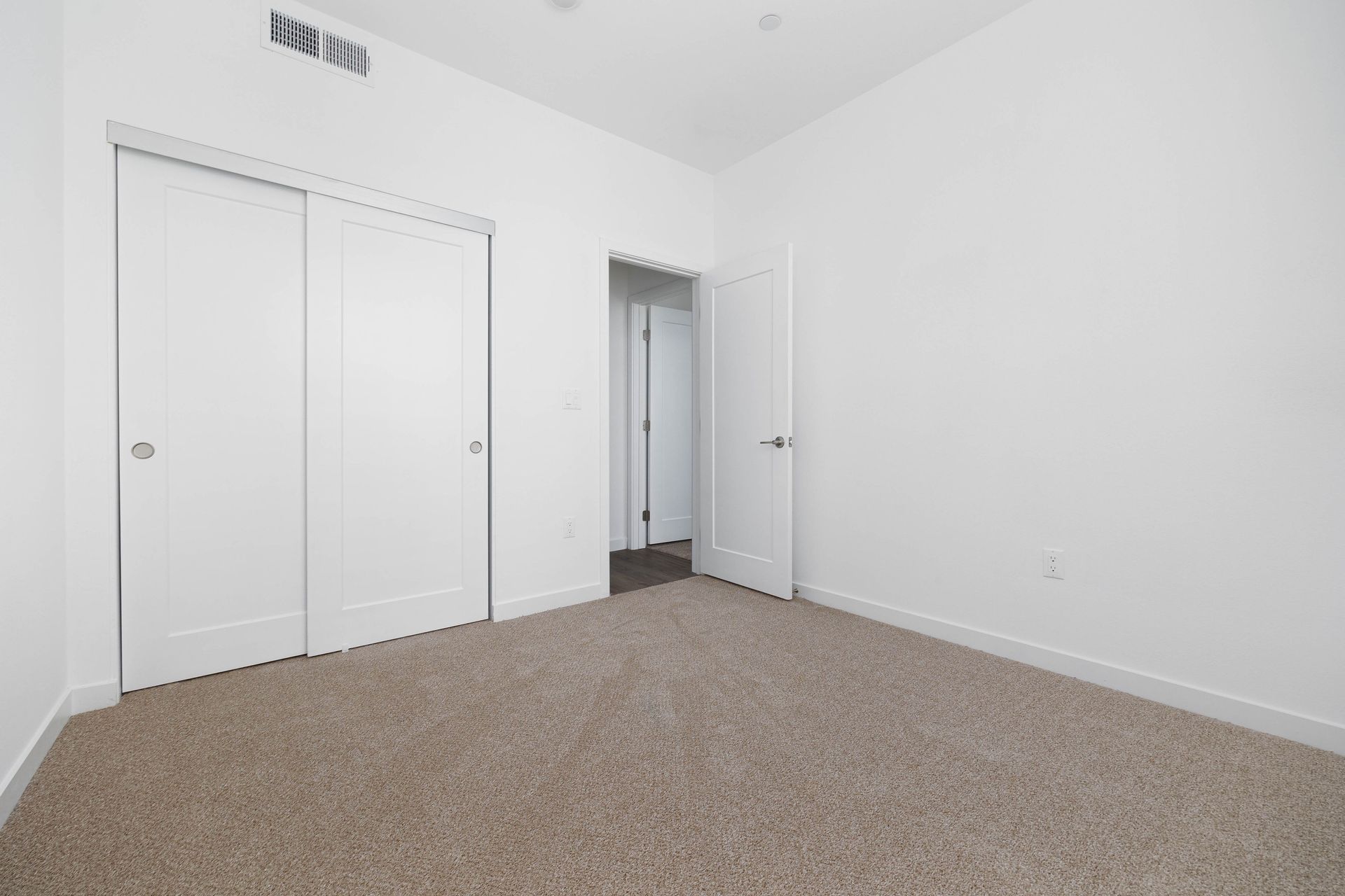 an empty bedroom with a carpeted floor and white walls .