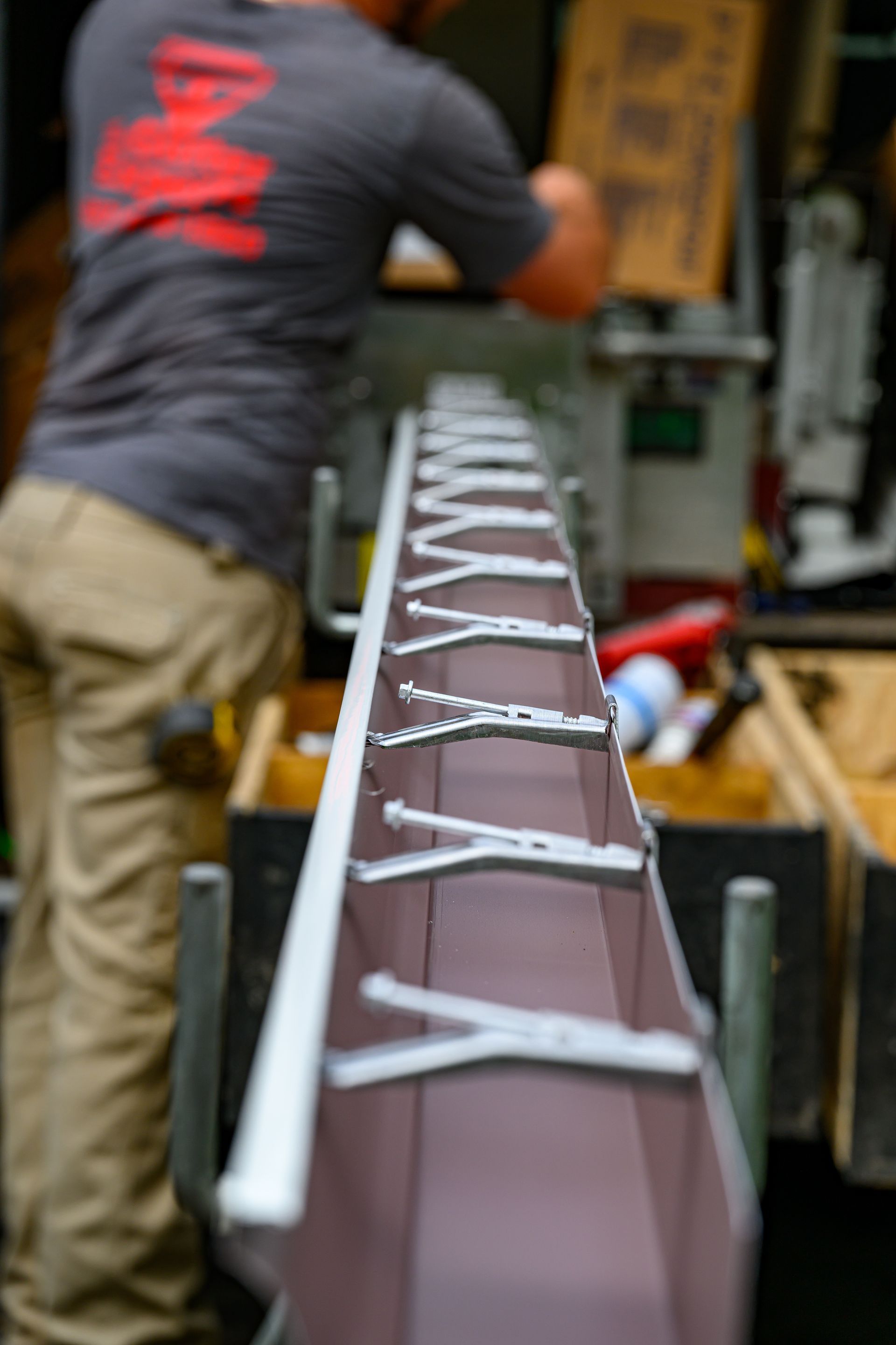 A man wearing a gray shirt with the letter m on the back is working on a piece of metal