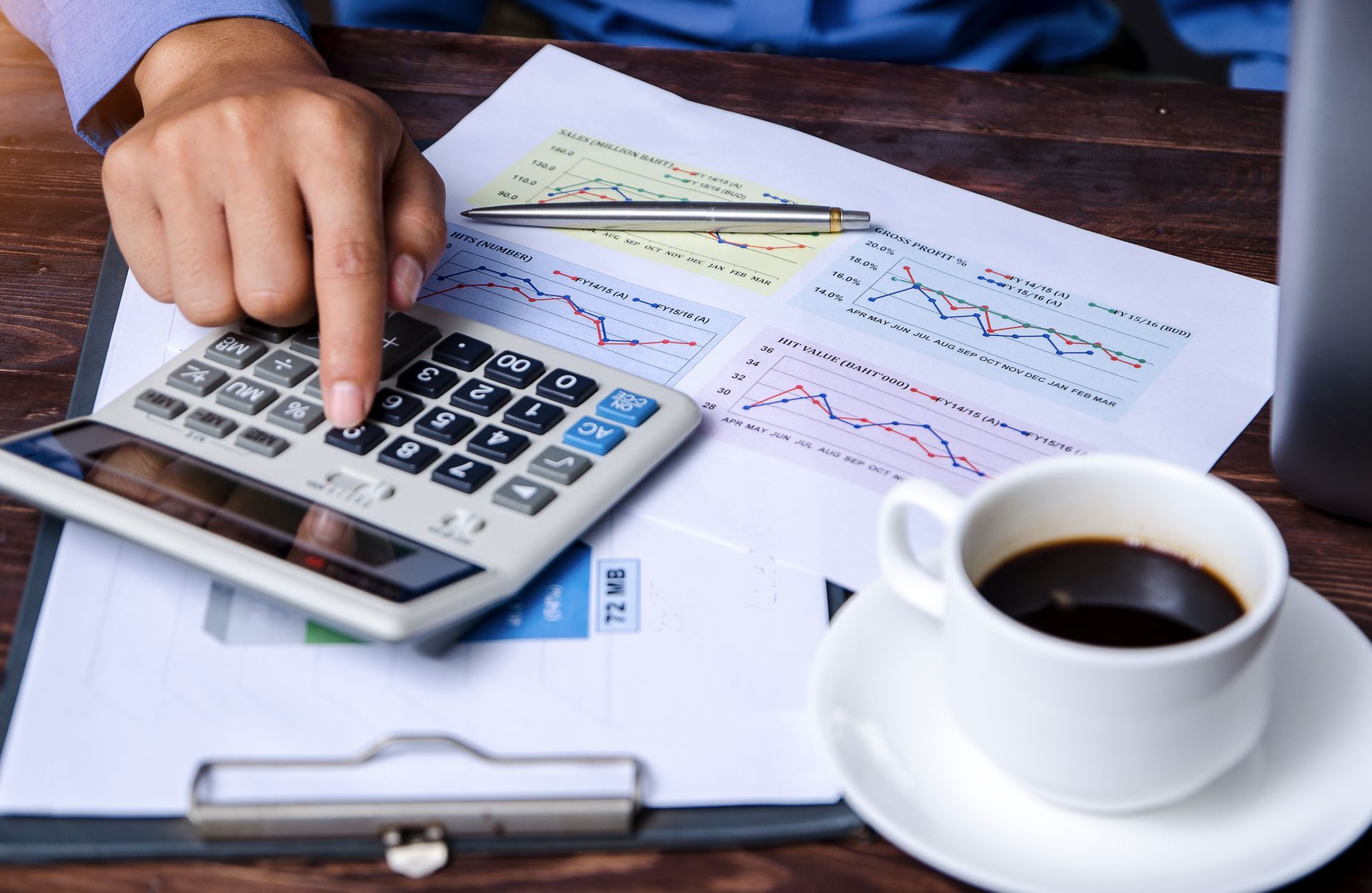 A person is using a calculator next to a cup of coffee.