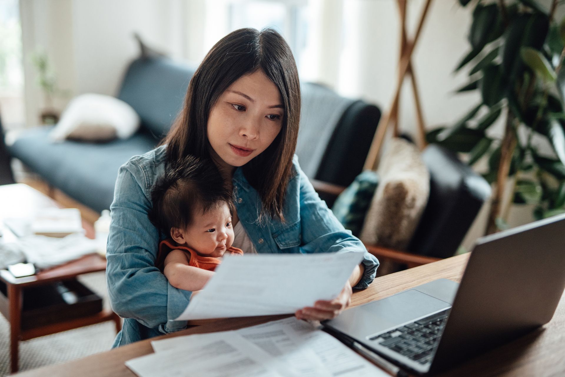 A woman is holding a baby while using a laptop computer.