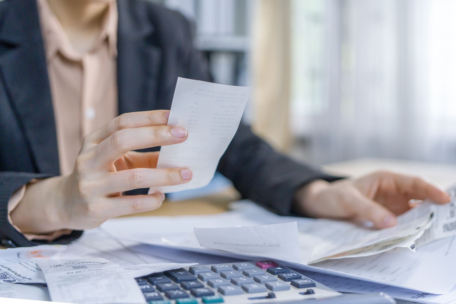 A woman is holding a receipt in her hand while sitting at a desk with a calculator.