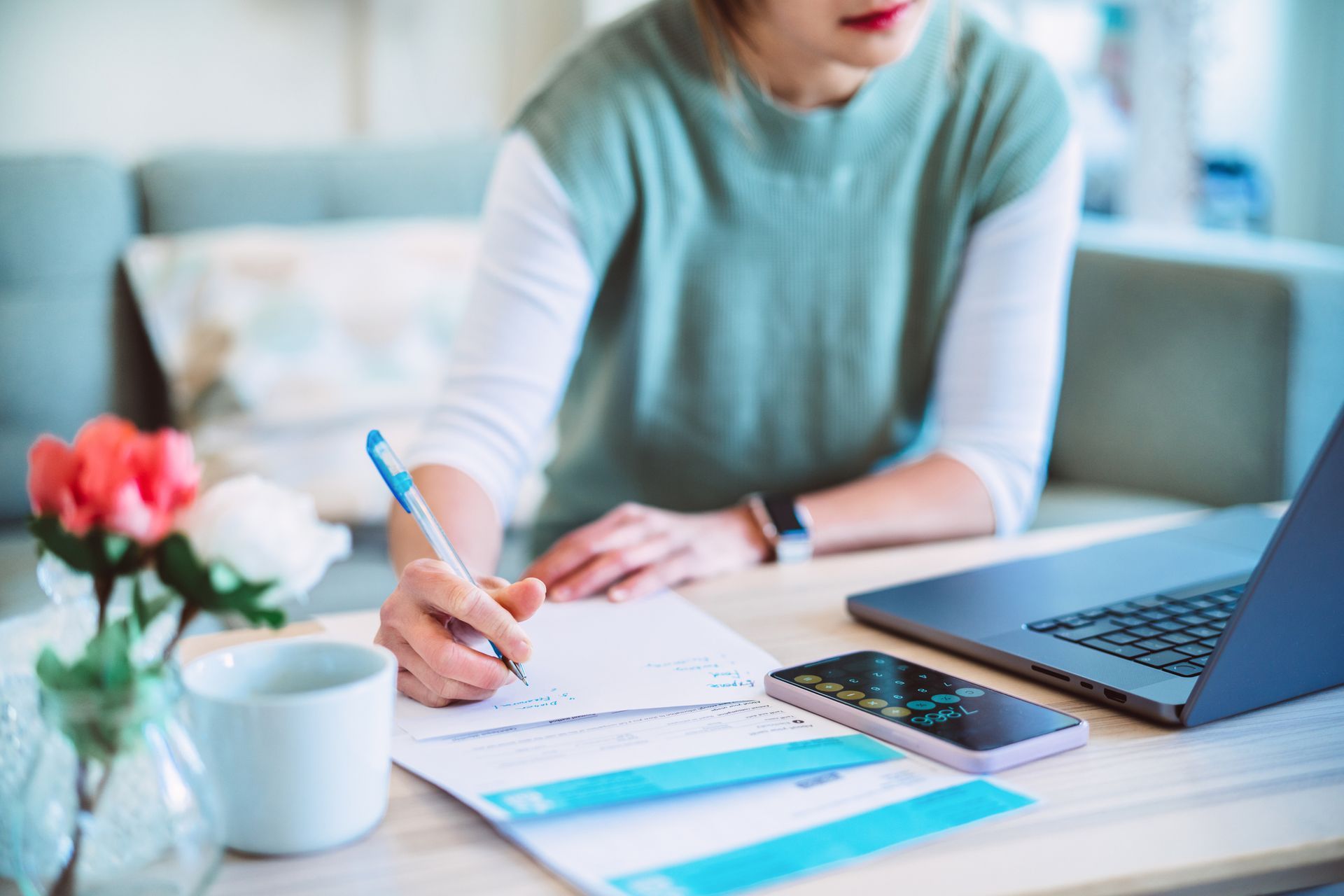 A woman is sitting at a table with a laptop and a cell phone.