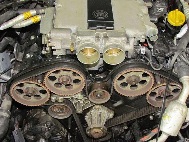 Car engine with exposed timing belts and pulleys, likely undergoing maintenance.