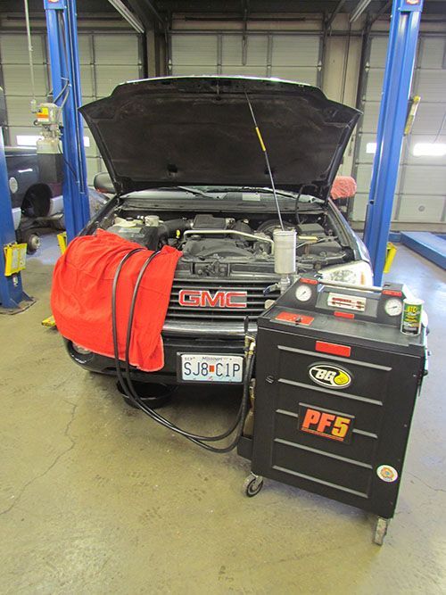 A GMC SUV with its hood open in a garage.  A red towel and black hoses connect to a black PFS5 machine.