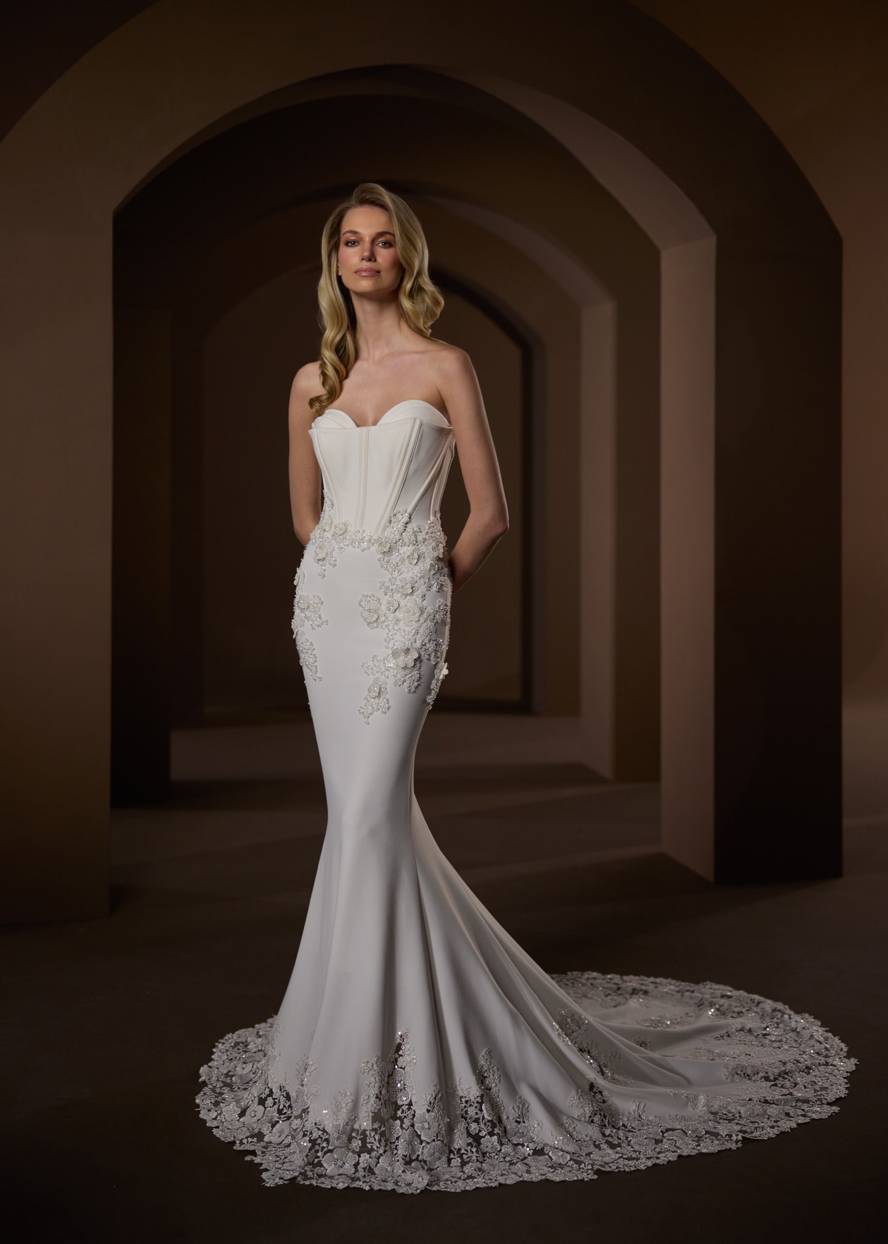 Woman in a white strapless mermaid wedding dress poses in an arched hallway.
