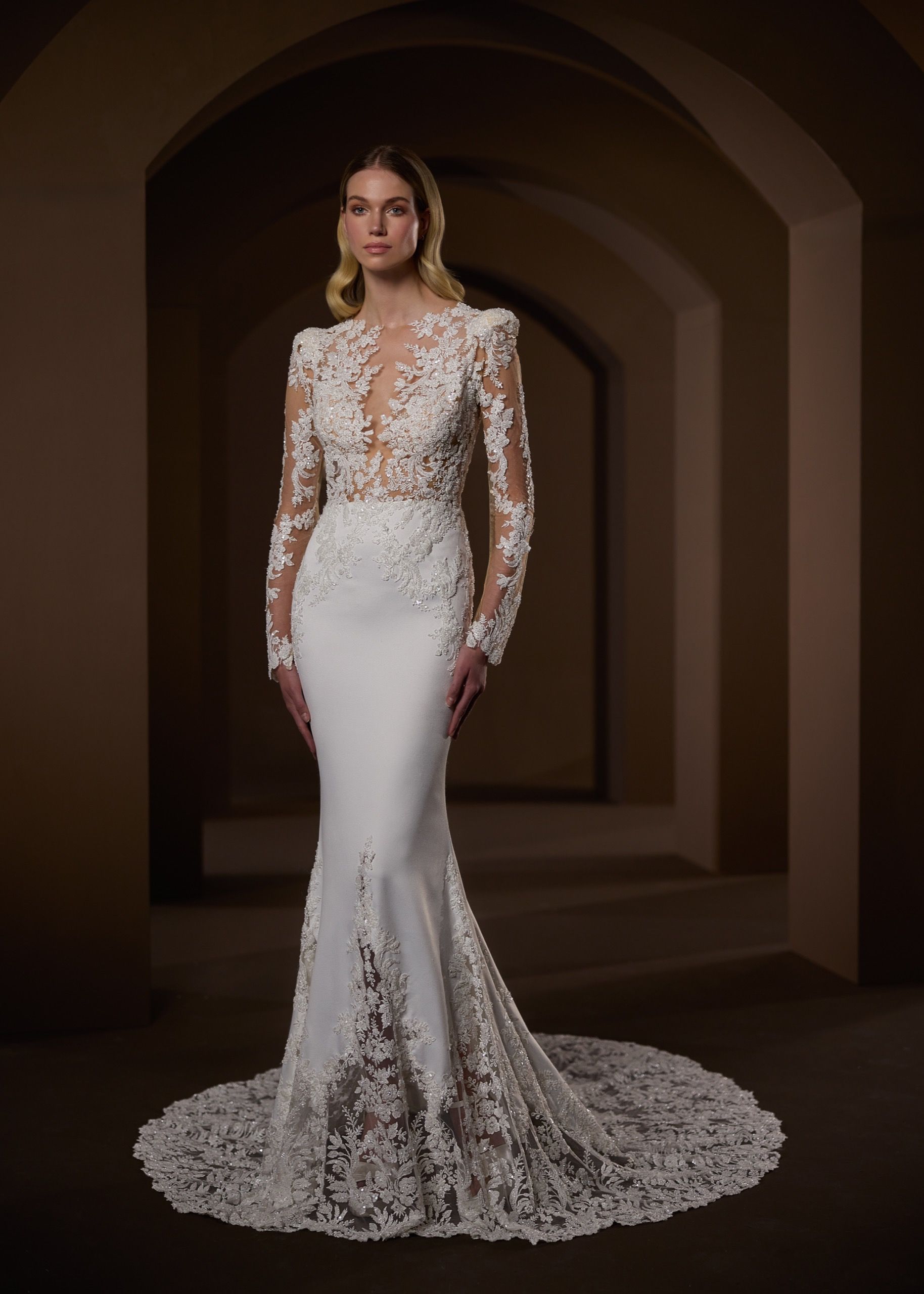 Woman in white wedding dress with long sleeves, intricate bodice, and mermaid skirt.