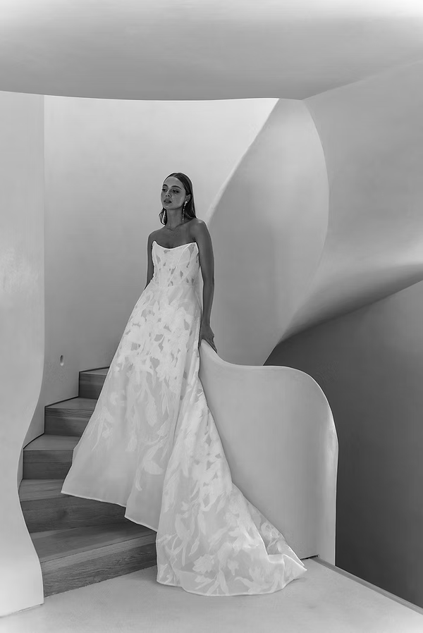 Woman in white wedding dress descends curved staircase.