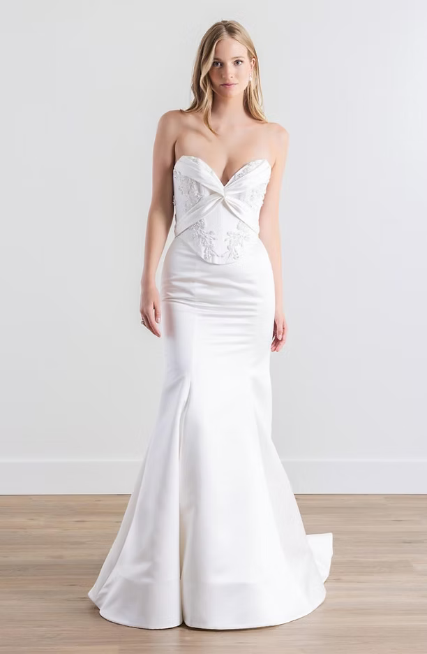 Woman in a white, strapless mermaid wedding dress poses against a white backdrop.