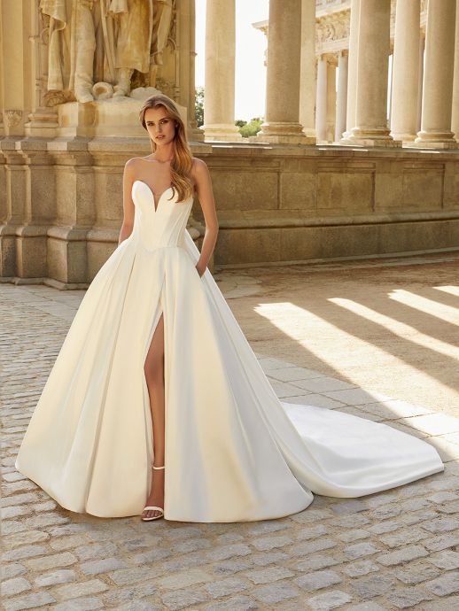 Woman in a strapless ivory wedding gown with high slit and long train, posing outdoors.
