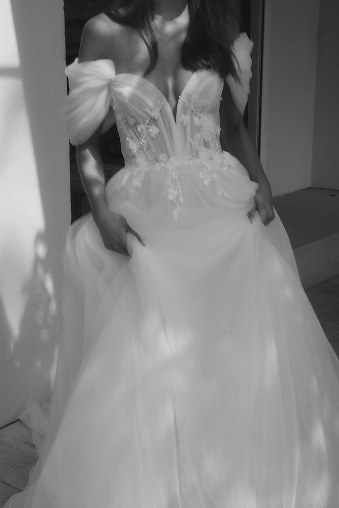 Woman in a white off-the-shoulder wedding dress, holding the skirt.