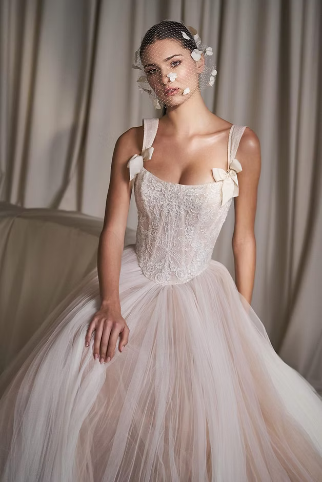 Woman in a white wedding dress with a tulle skirt and embellished bodice, standing against a neutral backdrop.