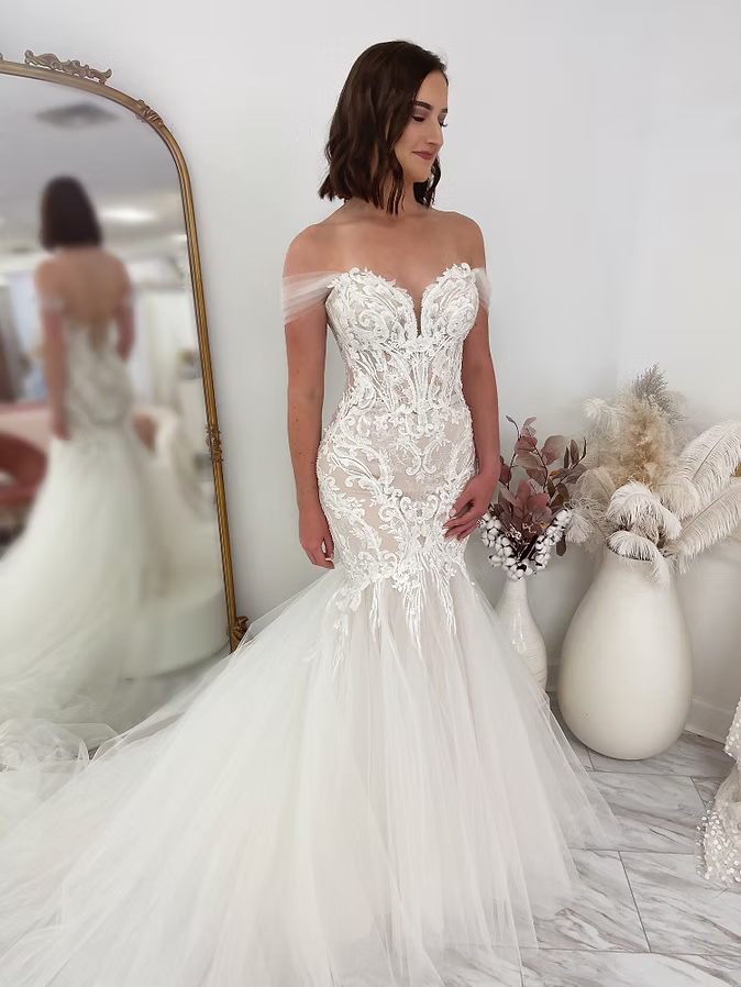 Woman in a white mermaid wedding dress with lace bodice, posing in a bridal shop.