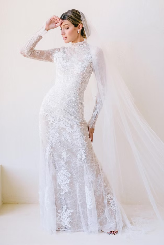 Bride in white lace gown with veil, posing in a studio.