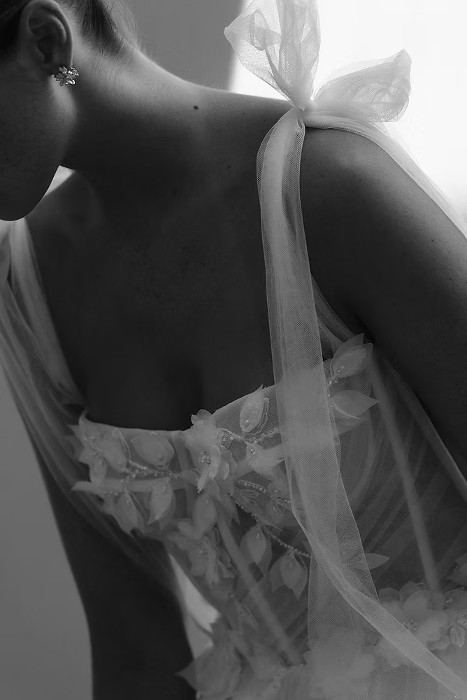 Woman in a white dress with floral accents, tied ribbon straps, and low back.