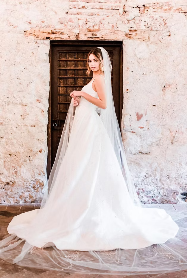 Bride in a white wedding dress with a veil stands in front of a dark wooden door, near a distressed wall.