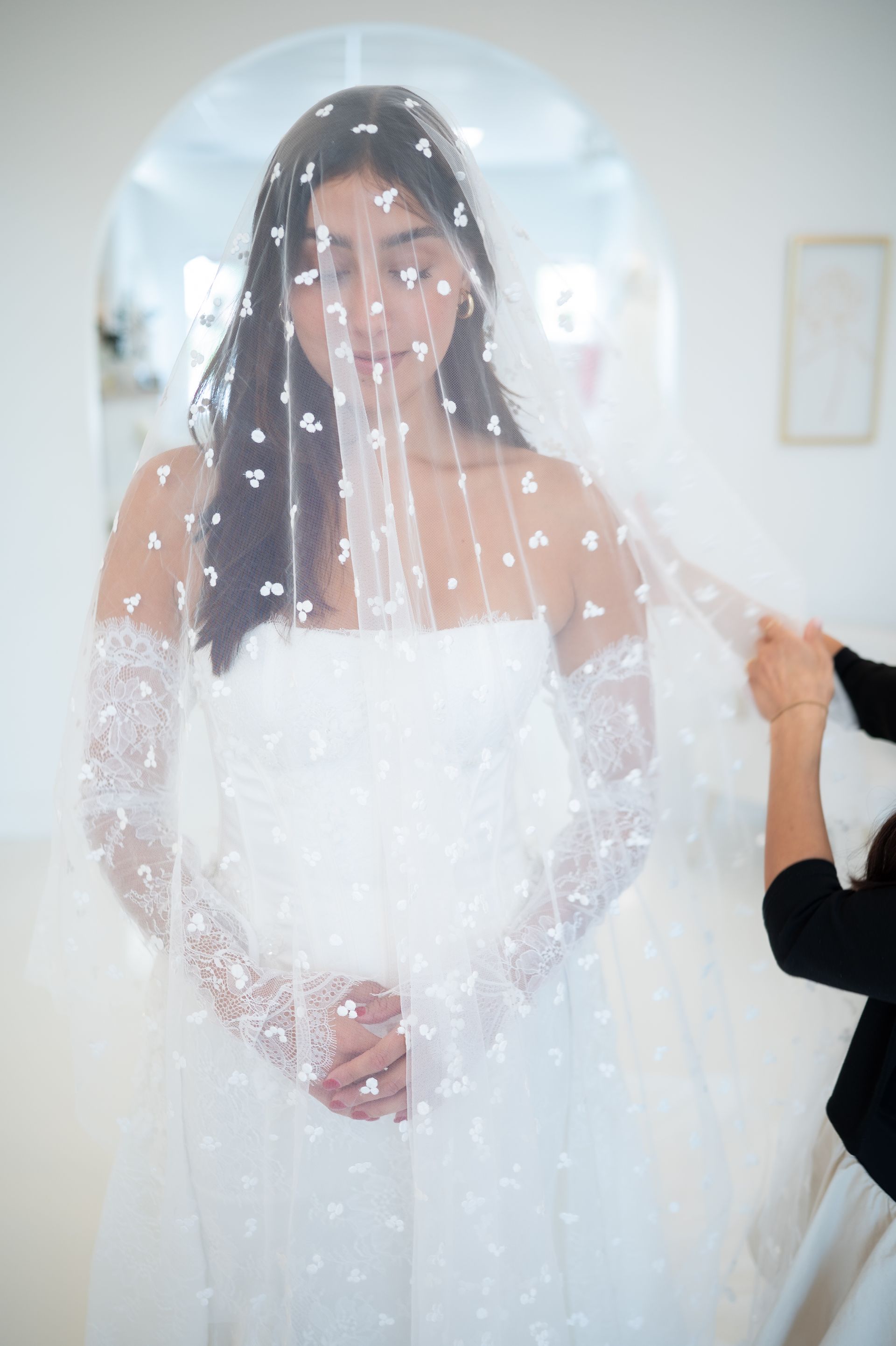Bride in white dress, veil with flower accents, hands holding veil.