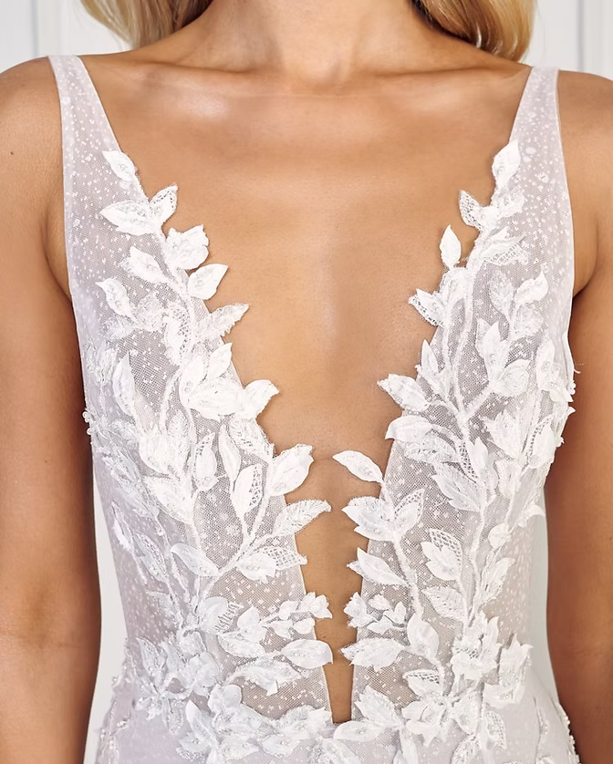 Woman in white bridal gown with deep V-neckline, floral lace detail.
